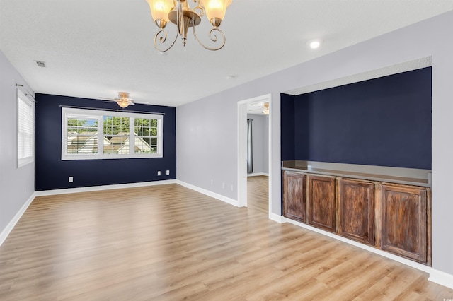 unfurnished room featuring ceiling fan with notable chandelier and light hardwood / wood-style flooring