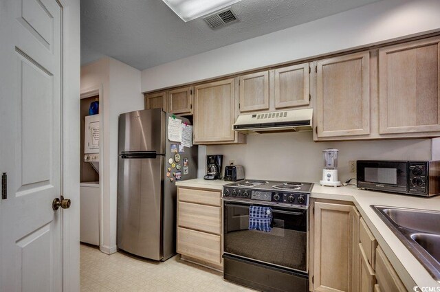kitchen featuring light floors, under cabinet range hood, a sink, stacked washer and dryer, and black appliances