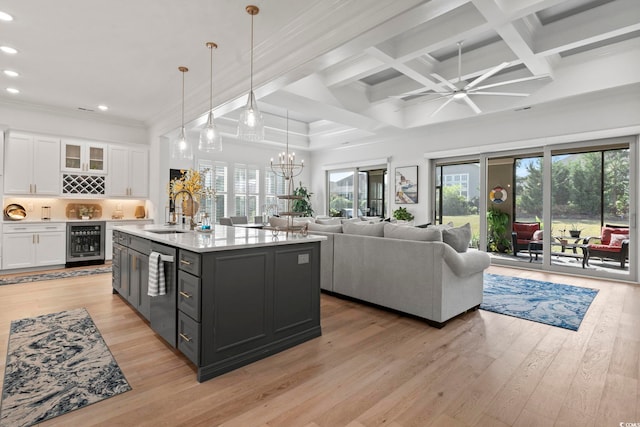 kitchen featuring wine cooler, hanging light fixtures, a center island with sink, white cabinetry, and light hardwood / wood-style floors