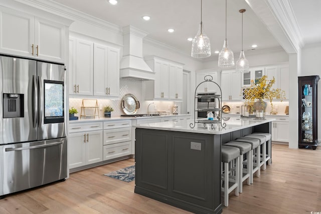 kitchen with light hardwood / wood-style flooring, a center island with sink, white cabinets, custom exhaust hood, and appliances with stainless steel finishes