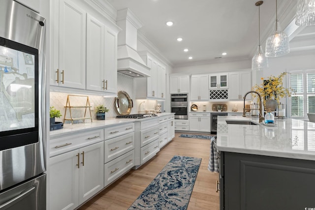 kitchen with white cabinets, appliances with stainless steel finishes, light hardwood / wood-style flooring, custom range hood, and sink