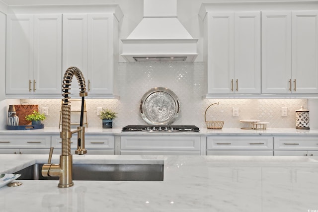 kitchen featuring decorative backsplash, white cabinetry, light stone countertops, custom range hood, and sink