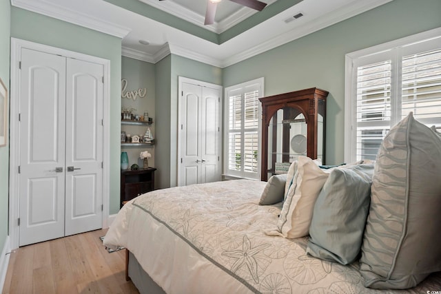 bedroom featuring light hardwood / wood-style flooring, ornamental molding, multiple closets, and ceiling fan