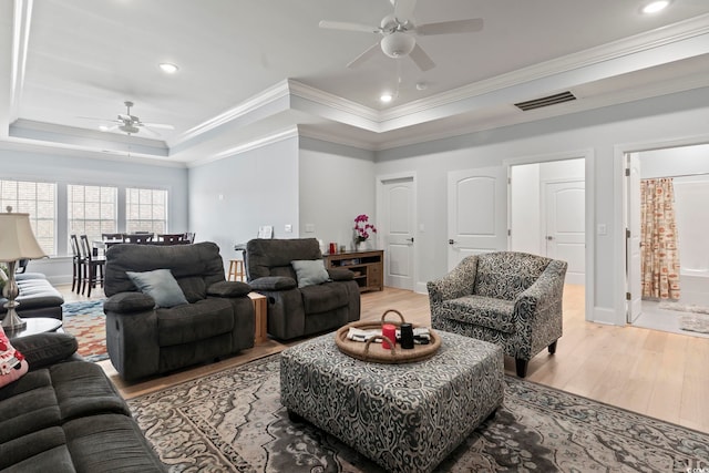 living room featuring light hardwood / wood-style flooring, ceiling fan, a tray ceiling, and crown molding