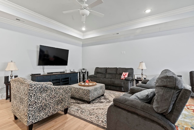 living room featuring a raised ceiling, ornamental molding, light wood-type flooring, and ceiling fan