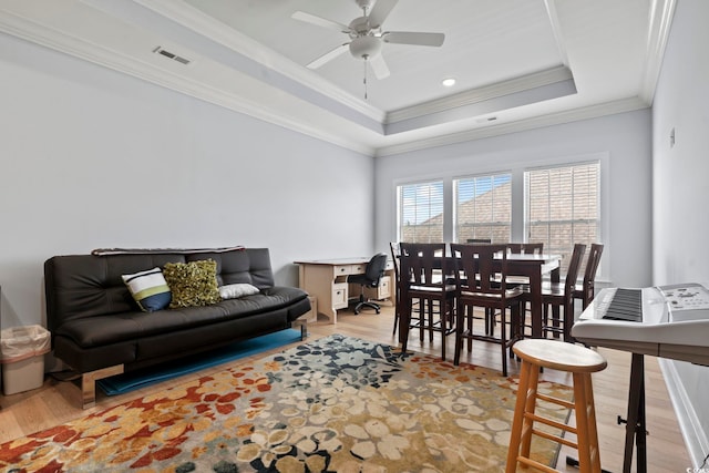 living room with ceiling fan, ornamental molding, a tray ceiling, and light wood-type flooring