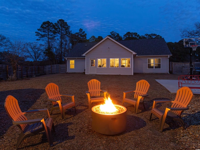 back of house at dusk with a patio, an outdoor fire pit, a shingled roof, and a fenced backyard