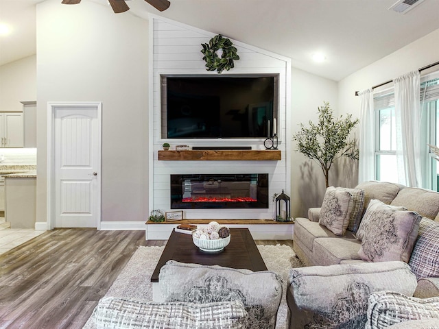 living room featuring ceiling fan, a fireplace, wood finished floors, visible vents, and vaulted ceiling