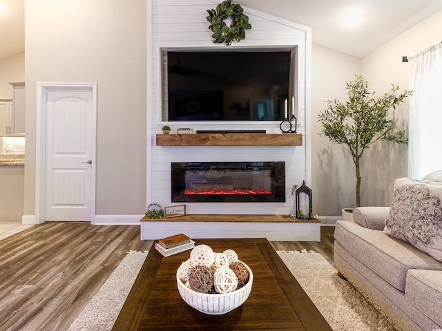 living room featuring vaulted ceiling, a fireplace, baseboards, and wood finished floors