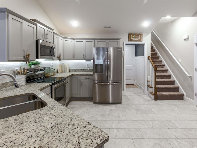 kitchen with appliances with stainless steel finishes, gray cabinets, a sink, and light stone countertops