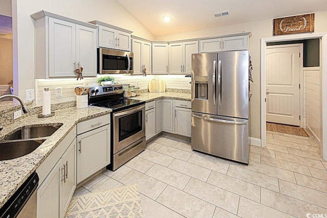 kitchen with stainless steel appliances, lofted ceiling, visible vents, a sink, and light stone countertops