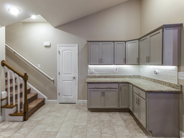 kitchen with light tile patterned floors, stone counters, vaulted ceiling, gray cabinets, and decorative backsplash