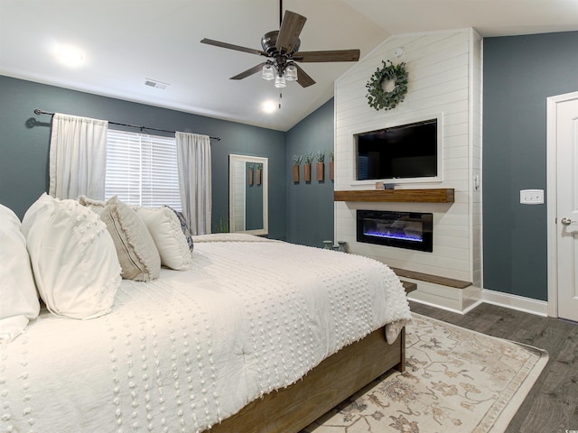 bedroom featuring dark wood finished floors, visible vents, a glass covered fireplace, vaulted ceiling, and baseboards