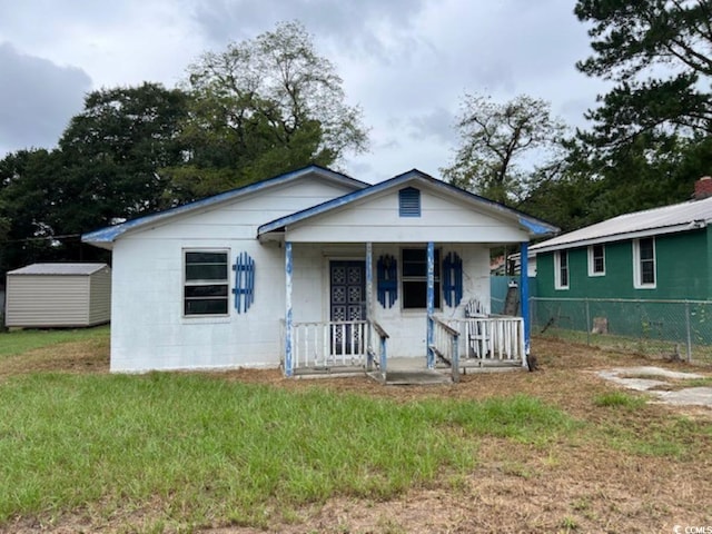 bungalow featuring a porch, a front lawn, and a storage unit