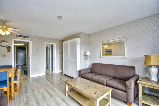 living room with light wood-type flooring, ceiling fan, and a textured ceiling