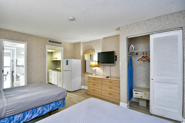 bedroom featuring a closet, light hardwood / wood-style floors, white refrigerator, a textured ceiling, and ensuite bath