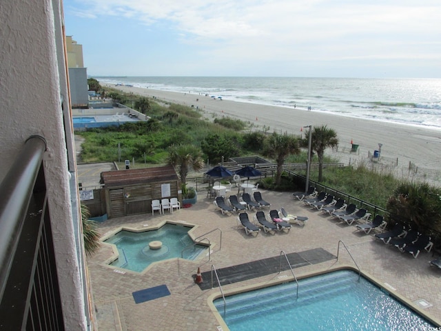 view of swimming pool with a patio, a water view, and a beach view