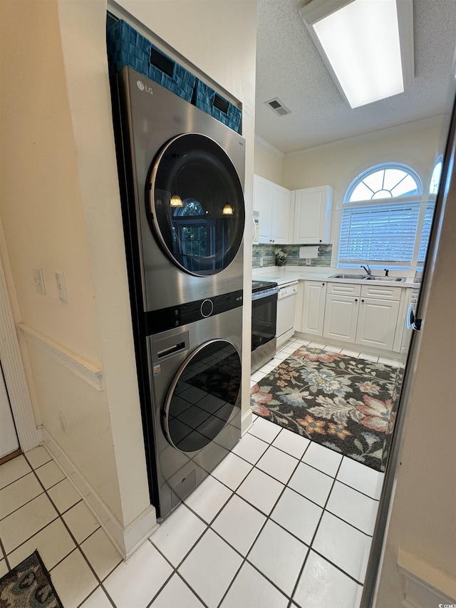 washroom with visible vents, laundry area, stacked washing maching and dryer, light tile patterned flooring, and a textured ceiling