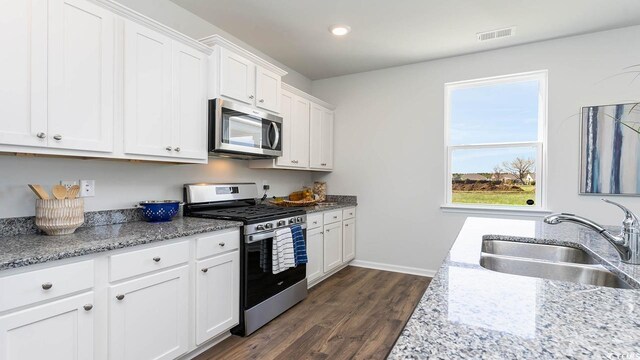 kitchen with light stone counters, white cabinets, sink, dark wood-type flooring, and stainless steel appliances