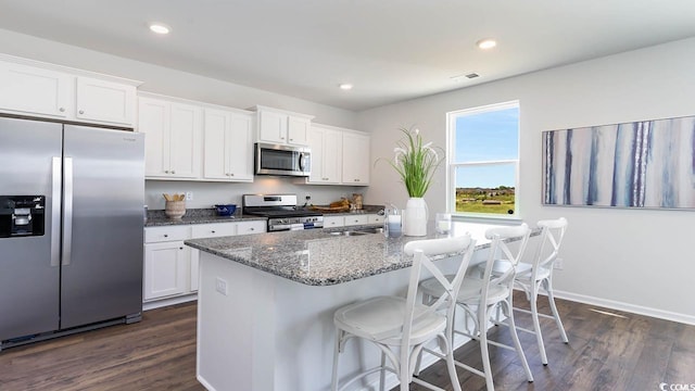 kitchen featuring a kitchen island with sink, dark wood-type flooring, white cabinetry, appliances with stainless steel finishes, and dark stone countertops