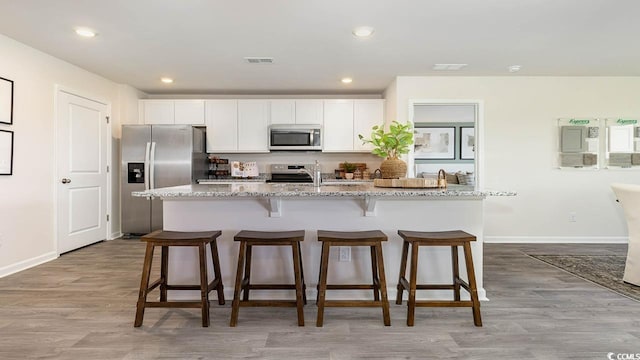 kitchen featuring white cabinetry, light stone countertops, stainless steel appliances, and an island with sink