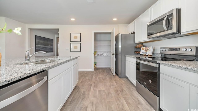 kitchen with sink, light wood-type flooring, light stone counters, white cabinetry, and stainless steel appliances