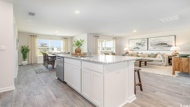 kitchen with white cabinetry, sink, light stone counters, light hardwood / wood-style flooring, and an island with sink