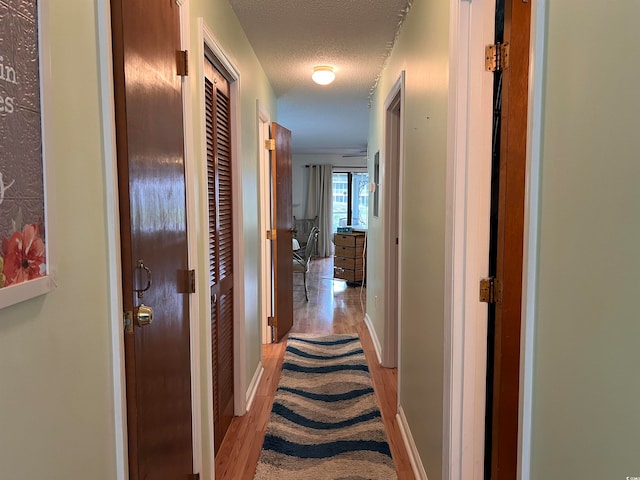 corridor with a textured ceiling and light wood-type flooring