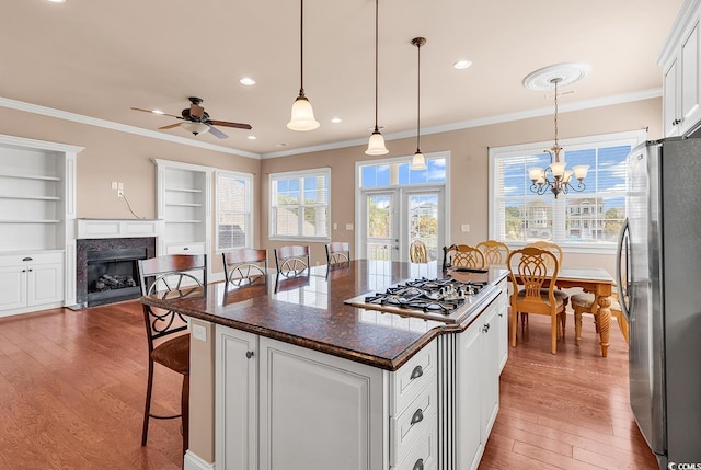 kitchen featuring ceiling fan with notable chandelier, appliances with stainless steel finishes, a center island, hanging light fixtures, and light wood-type flooring