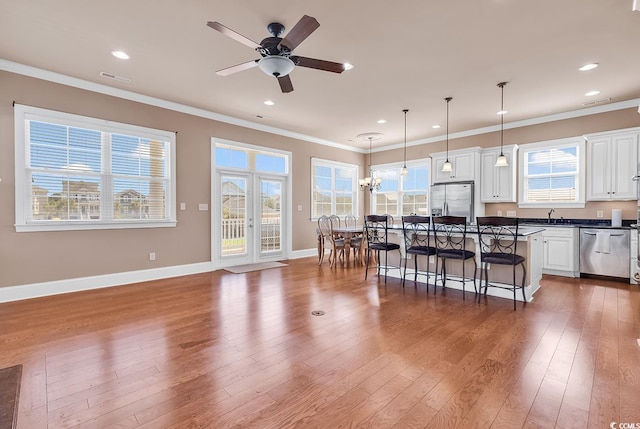 kitchen with white cabinets, ceiling fan with notable chandelier, stainless steel appliances, pendant lighting, and a kitchen bar