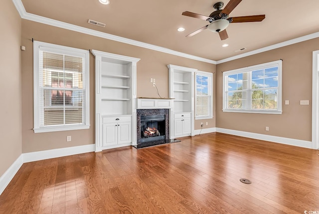 unfurnished living room featuring a high end fireplace, ornamental molding, wood-type flooring, and ceiling fan