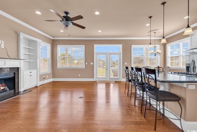 kitchen featuring a fireplace, light wood-type flooring, ceiling fan with notable chandelier, and a kitchen bar