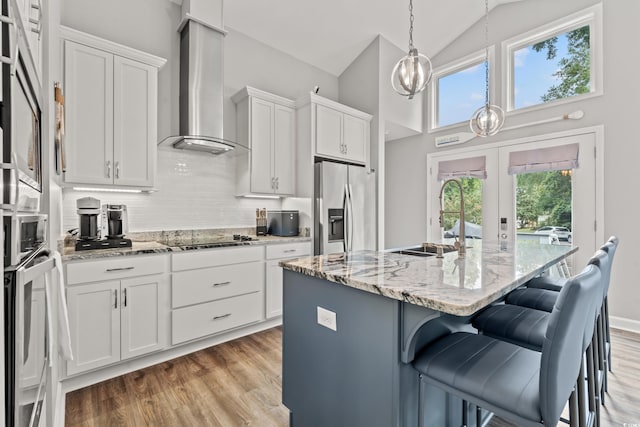 kitchen featuring a center island with sink, plenty of natural light, stainless steel fridge, and wall chimney range hood