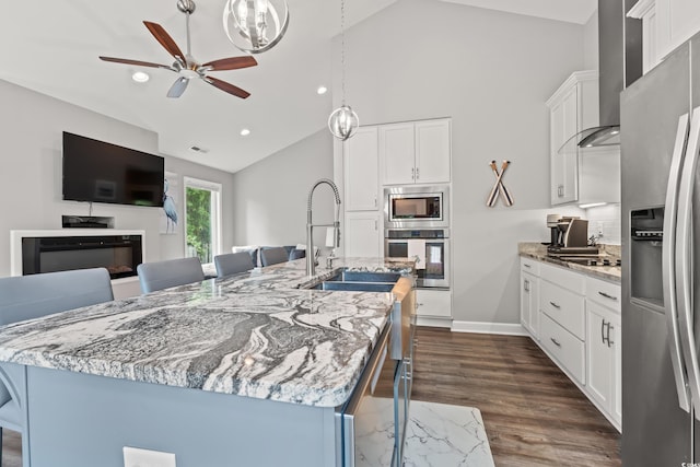 kitchen featuring pendant lighting, stainless steel appliances, light stone countertops, a center island with sink, and wall chimney range hood