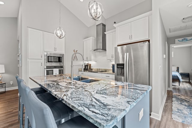 kitchen with appliances with stainless steel finishes, wall chimney exhaust hood, and a kitchen island with sink