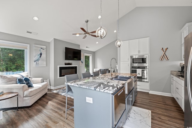 kitchen featuring appliances with stainless steel finishes, light stone counters, dark hardwood / wood-style floors, a kitchen island with sink, and a breakfast bar