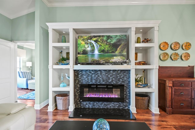 living room with hardwood / wood-style floors, built in shelves, ornamental molding, and a tiled fireplace