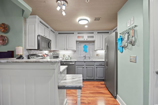 kitchen with stainless steel appliances, light hardwood / wood-style floors, tasteful backsplash, and sink