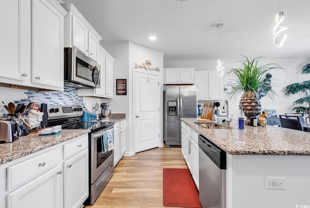 kitchen featuring white cabinets, hanging light fixtures, appliances with stainless steel finishes, sink, and a kitchen island with sink