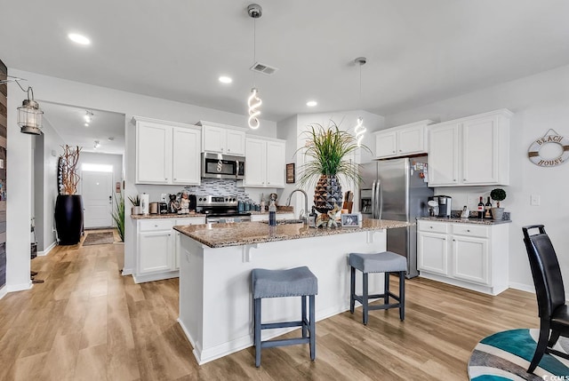 kitchen featuring decorative light fixtures, white cabinets, appliances with stainless steel finishes, and a center island with sink