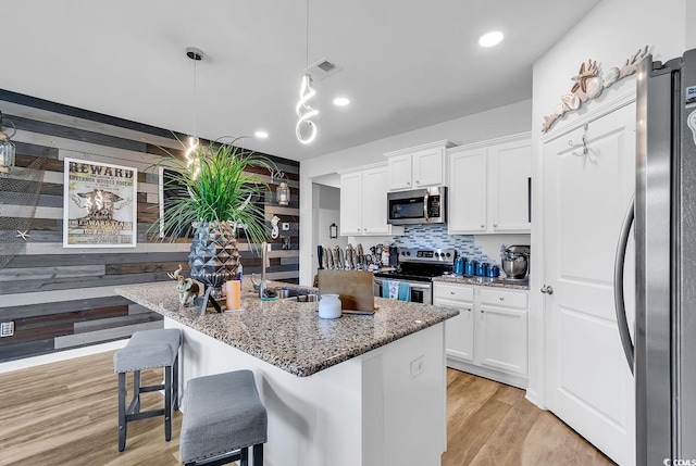 kitchen with a breakfast bar area, appliances with stainless steel finishes, an island with sink, light wood-type flooring, and white cabinets