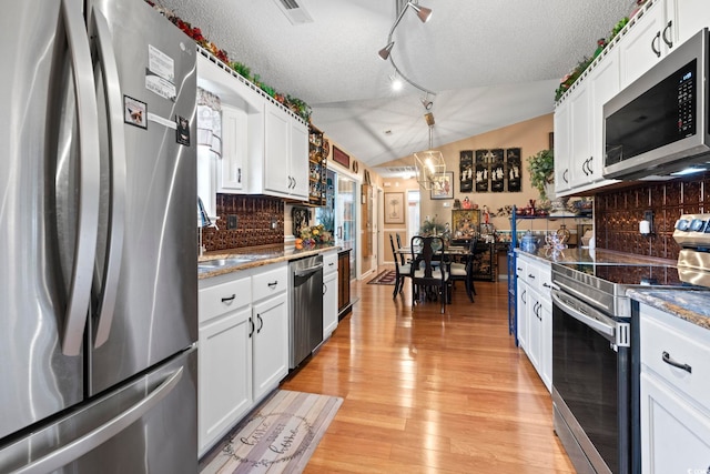 kitchen featuring a textured ceiling, vaulted ceiling, light hardwood / wood-style floors, stainless steel appliances, and white cabinetry