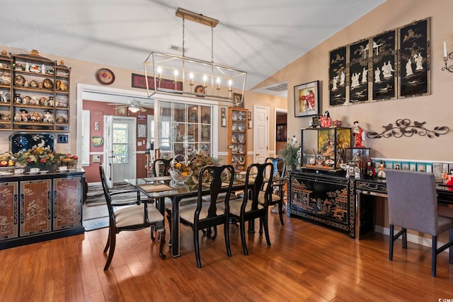 dining area featuring ceiling fan with notable chandelier, lofted ceiling, wood-type flooring, and a textured ceiling