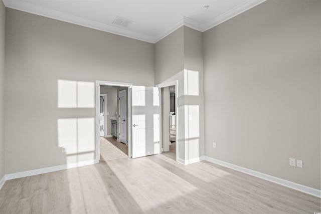 spare room featuring a towering ceiling, light hardwood / wood-style flooring, and ornamental molding