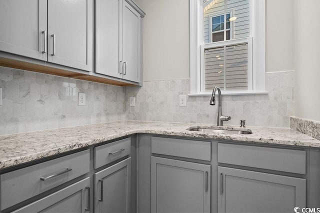 kitchen with gray cabinets, light stone countertops, sink, and decorative backsplash