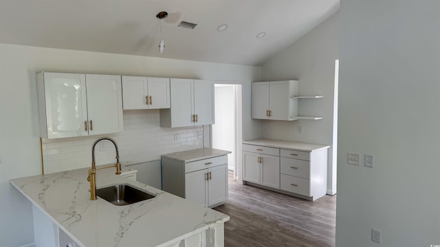 kitchen with hardwood / wood-style floors, sink, vaulted ceiling, light stone countertops, and white cabinetry