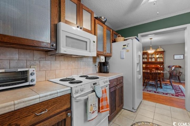 kitchen featuring crown molding, white appliances, light hardwood / wood-style flooring, a textured ceiling, and tile counters