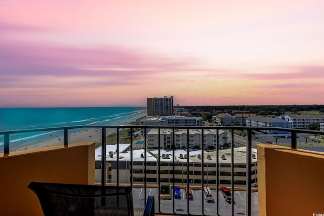 balcony at dusk featuring a view of the beach and a water view