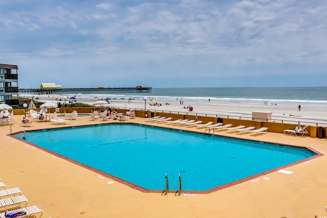 view of pool featuring a patio area, a water view, and a view of the beach