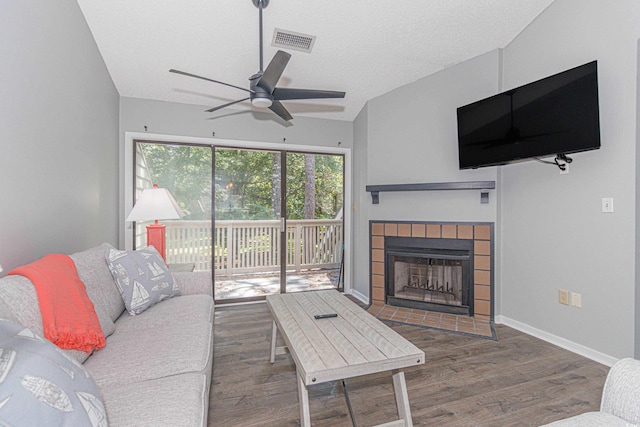 living room featuring a textured ceiling, a tile fireplace, vaulted ceiling, ceiling fan, and dark wood-type flooring